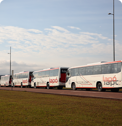 Fila de ônibus brancos da empresa Iapó estacionados em um pátio em um dia claro.